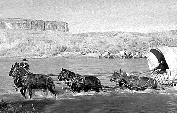 A six horse team pulls a wagon through a river