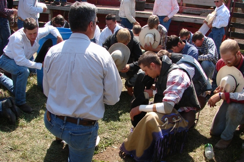 A sky pilot praying with rodeo contestants