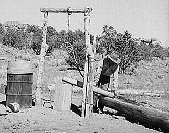 Faro Caudill pouring water from his well into watering trough made of hollowed-out log. Pie Town, New Mexico