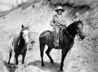 Chief Jim James shown riding a horse and leading another horse
